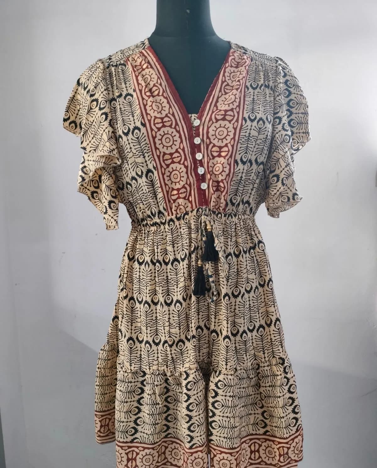 Front view of a cream, black and maroon block-print flutter-sleeve tiered mini dress on a dress form