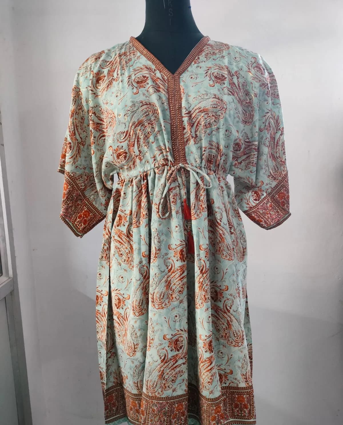 Front view of a mint and rust border-print paisley kaftan with tie waist on a dress form