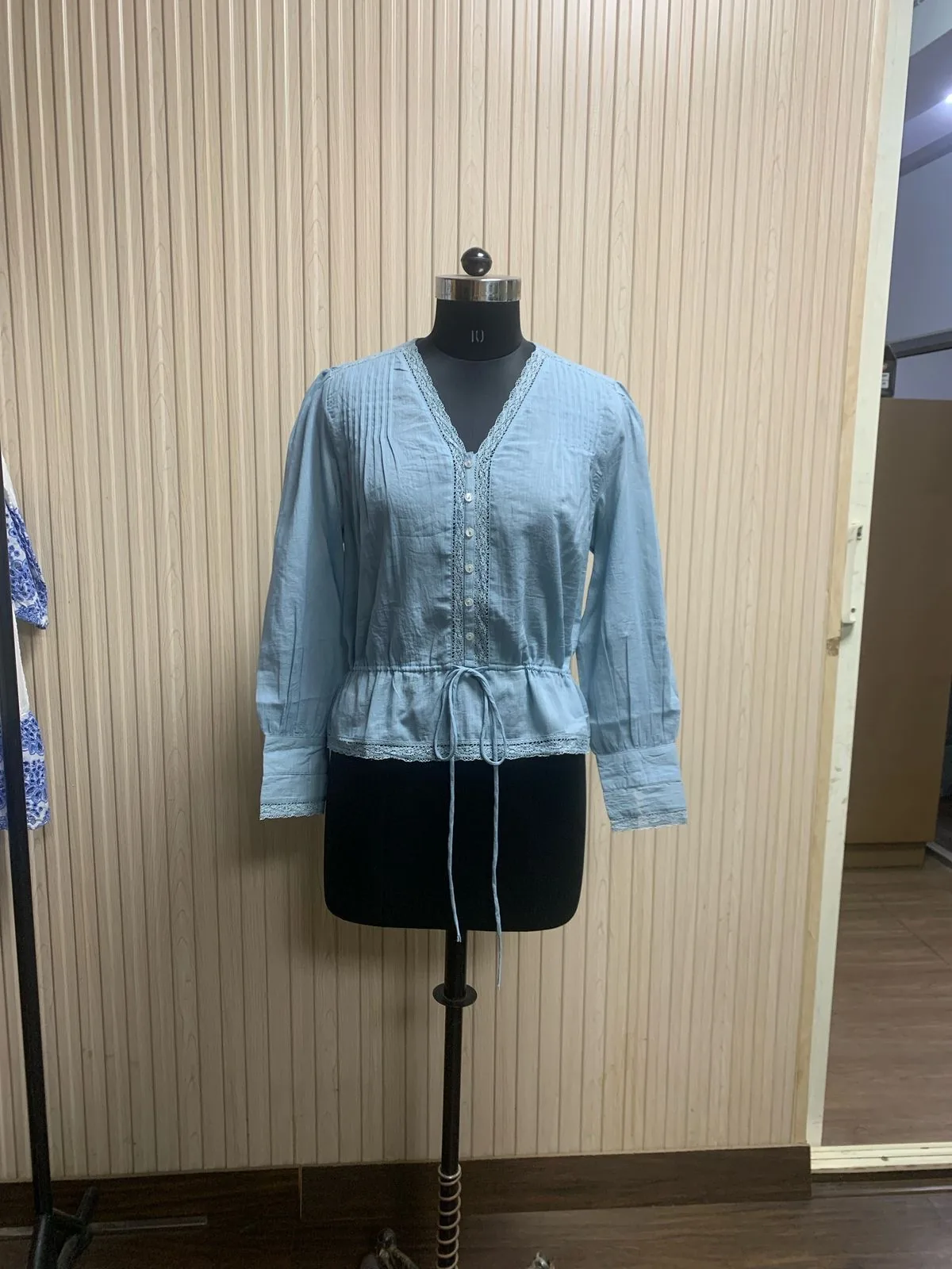 Front view of a light blue chambray drawstring-waist blouse on a dress form