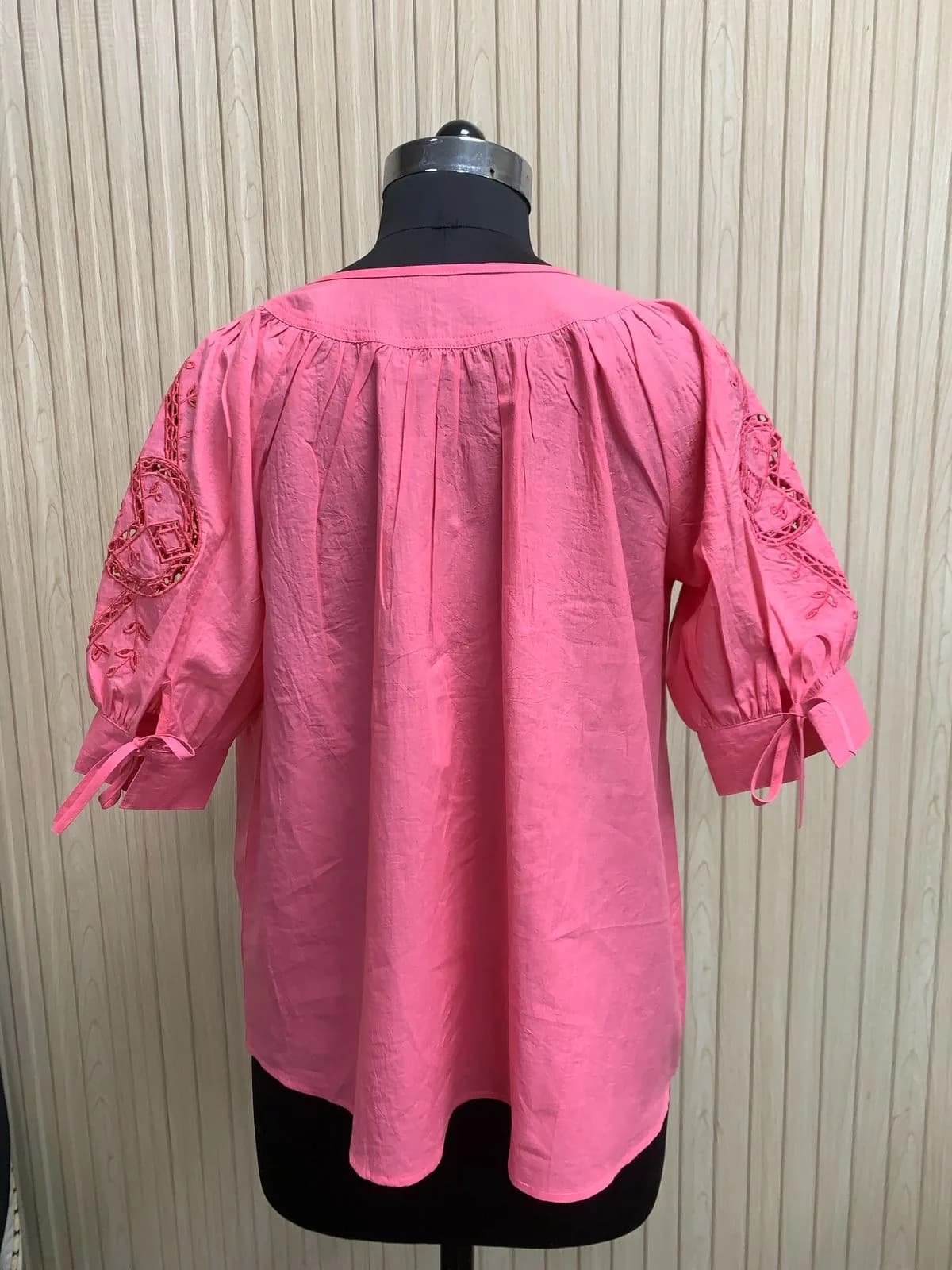 Back view of a pink cutwork-sleeve blouse with tie cuffs on a dress form