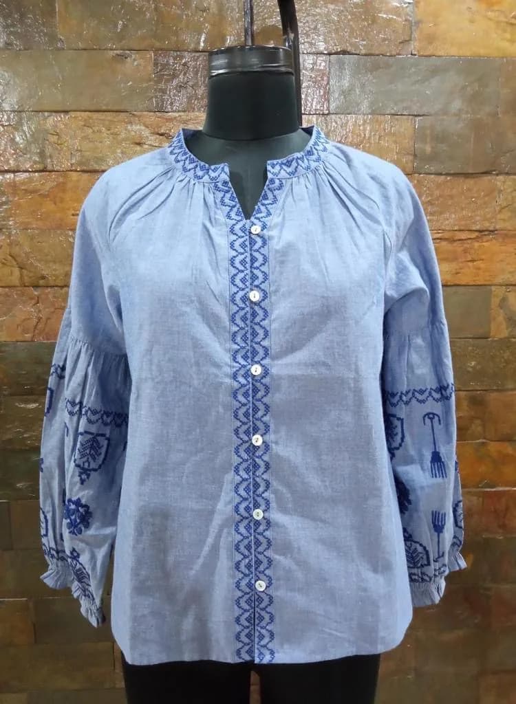 Front view of a light blue embroidered chambray blouse on a dress form