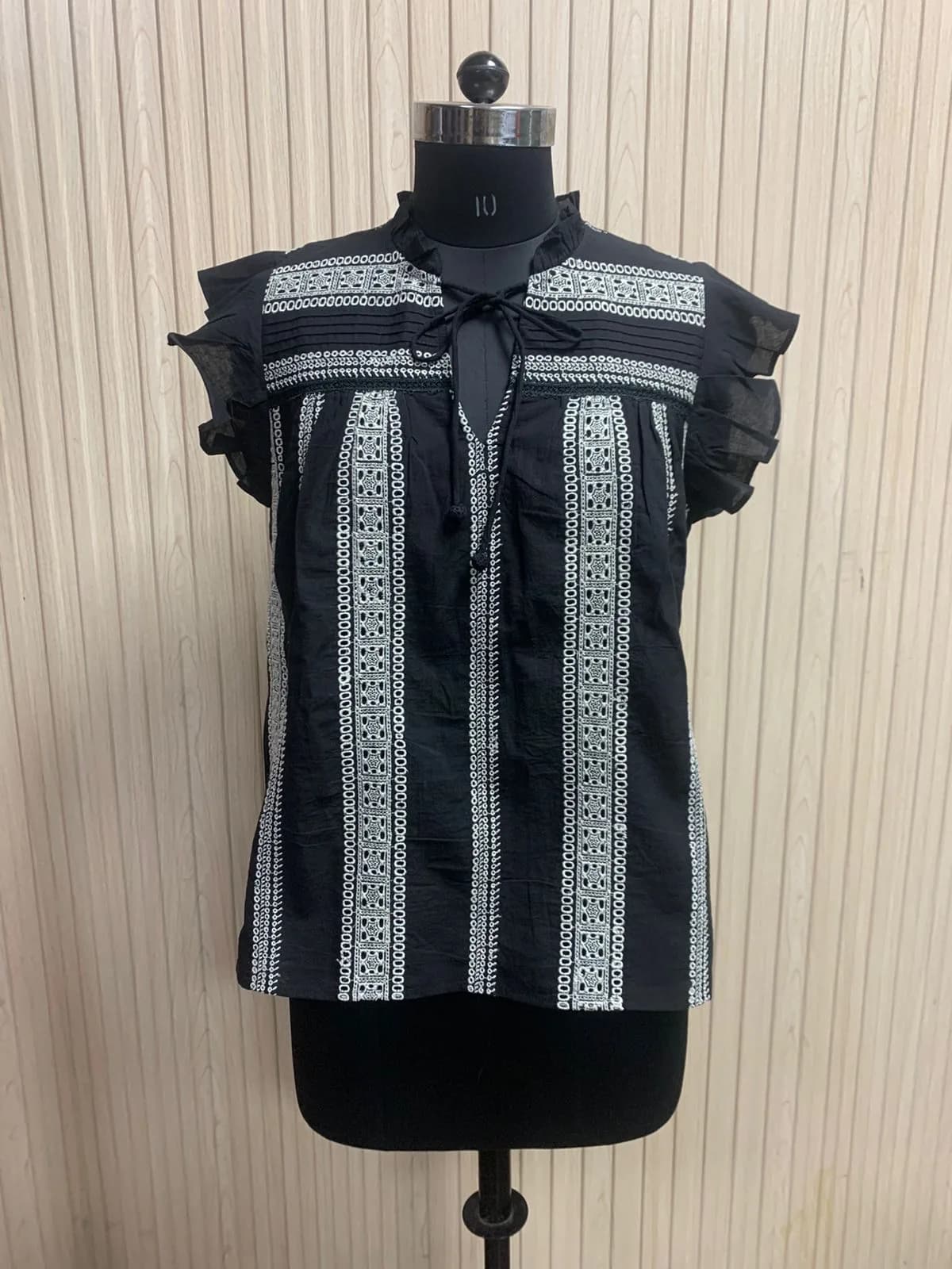 Front view of a black and white embroidered-stripe flutter-sleeve blouse on a dress form
