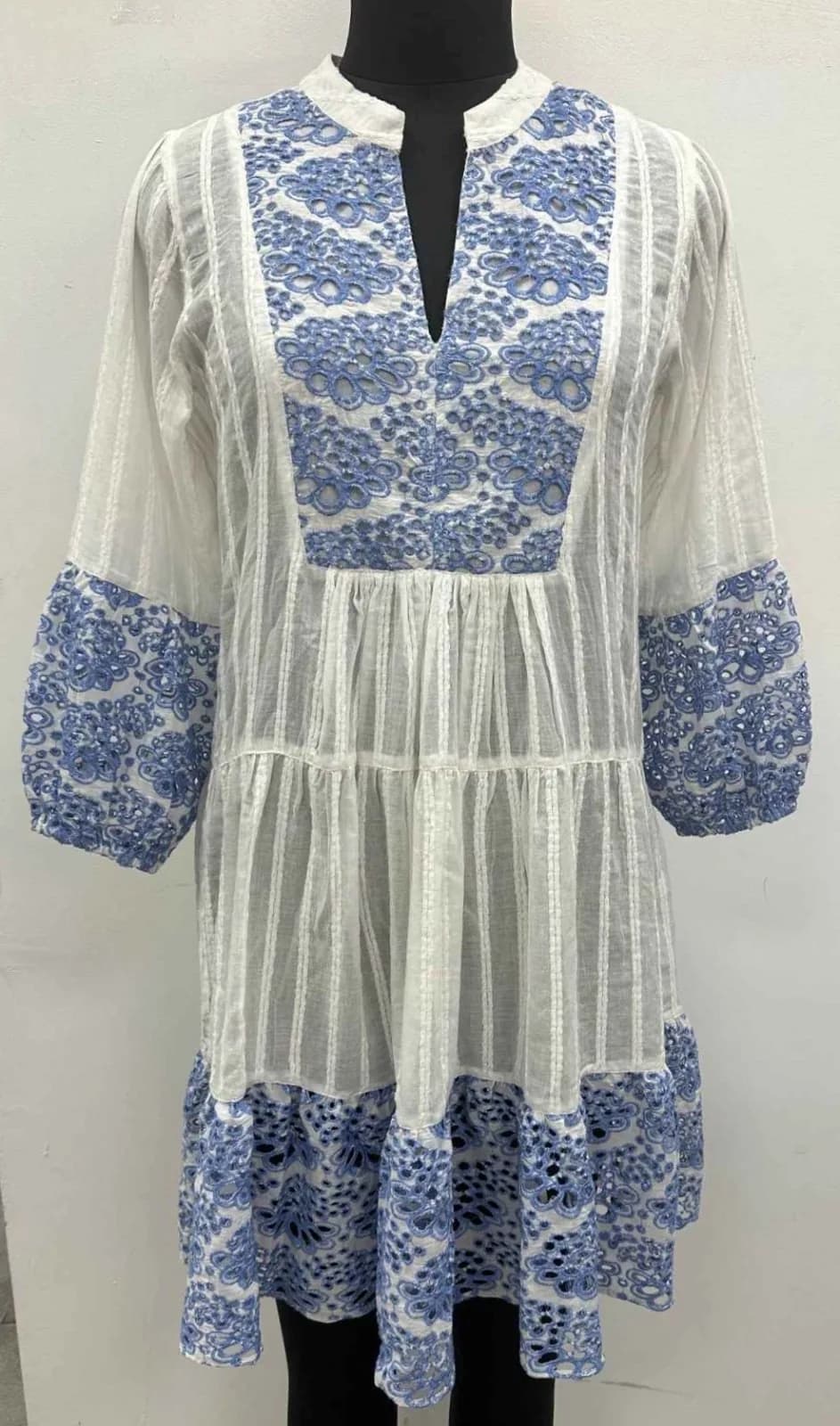 Front view of a white and blue embroidered tiered tunic dress with bell sleeves on a dress form