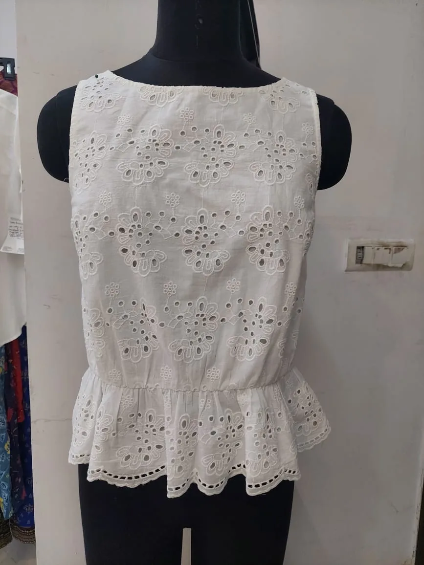 Front view of a white eyelet sleeveless peplum top on a dress form