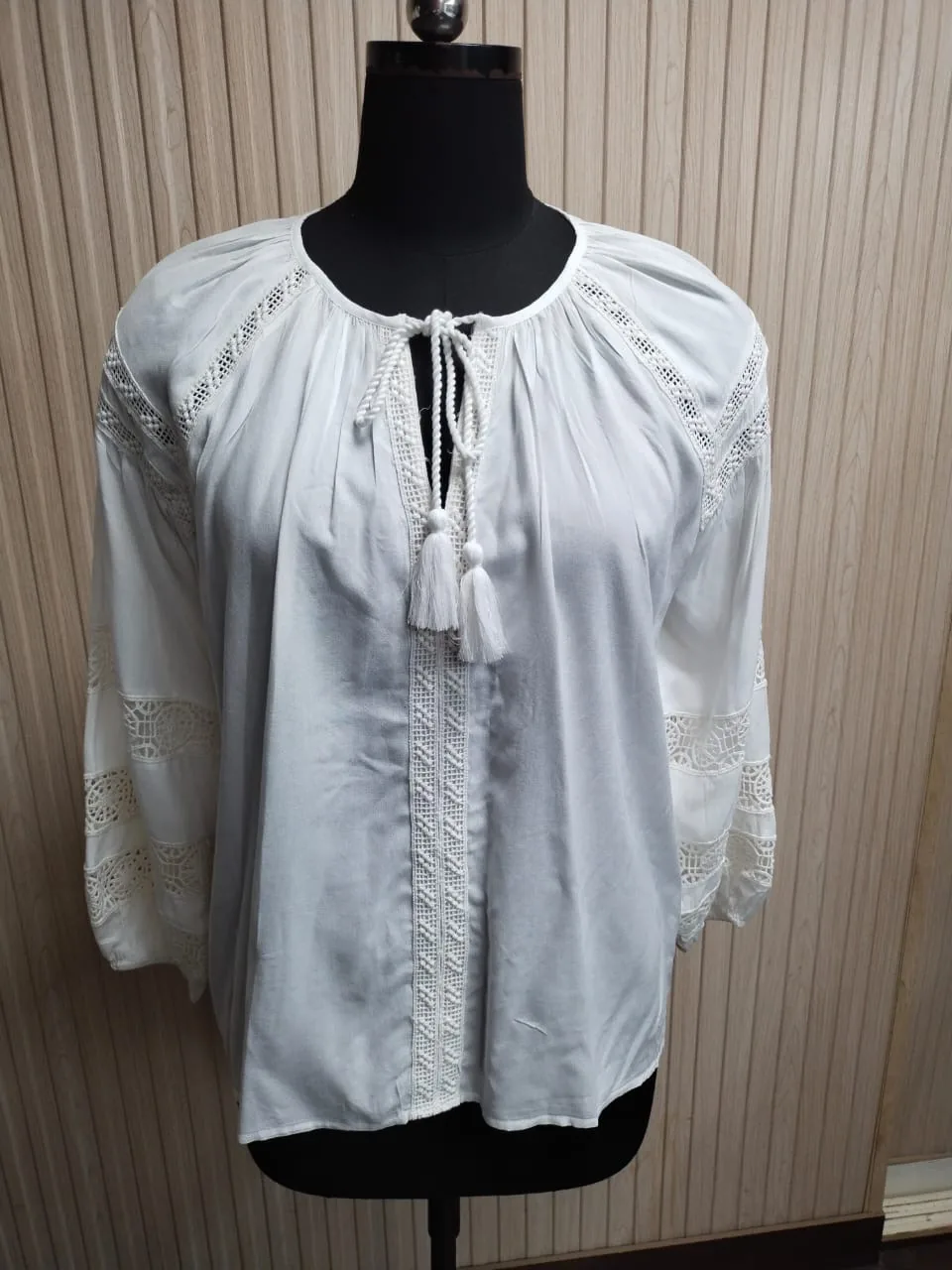 Front view of a white lace-insertion peasant blouse with tassels on a dress form