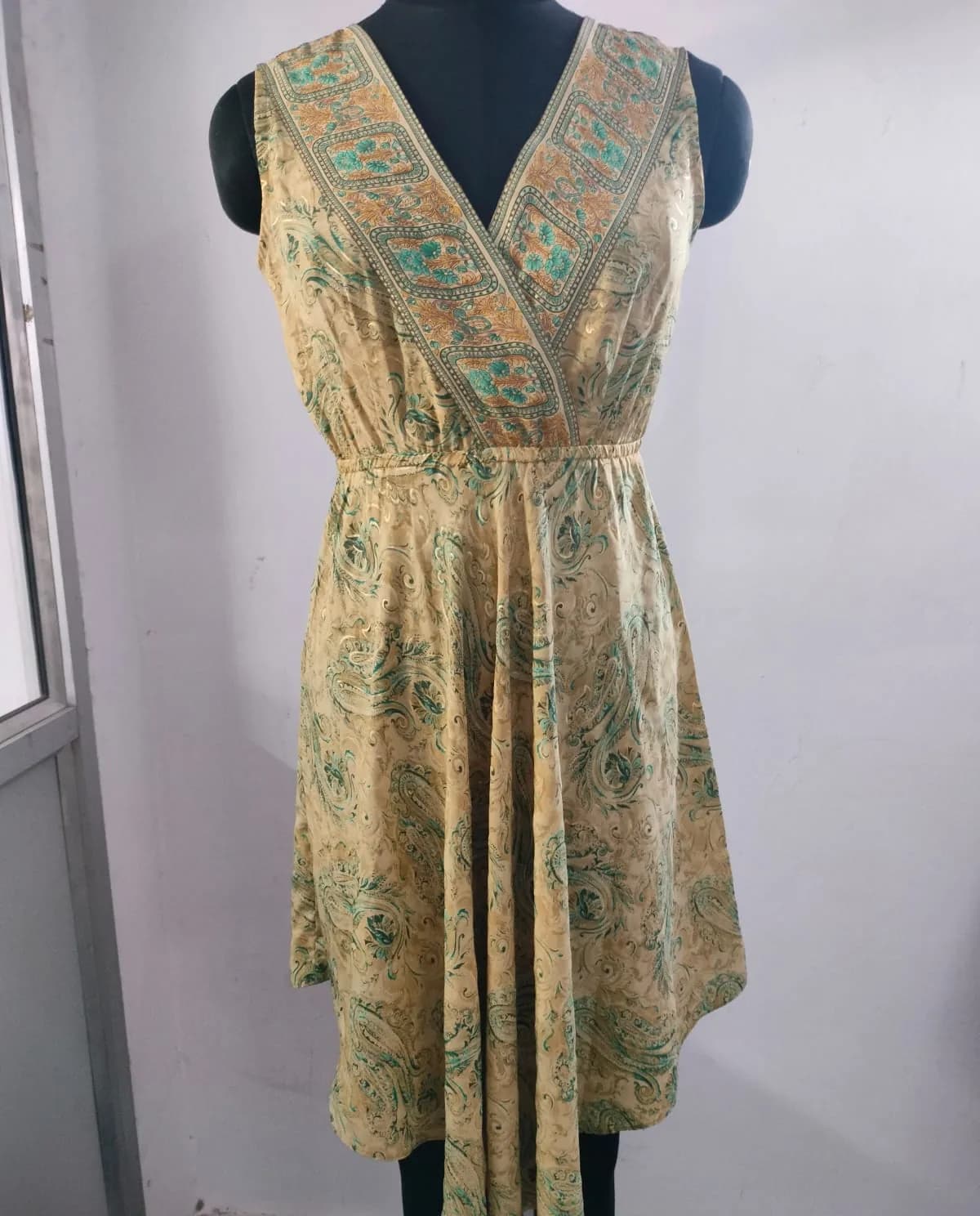 Front view of a gold and green paisley sleeveless wrap midi dress on a dress form