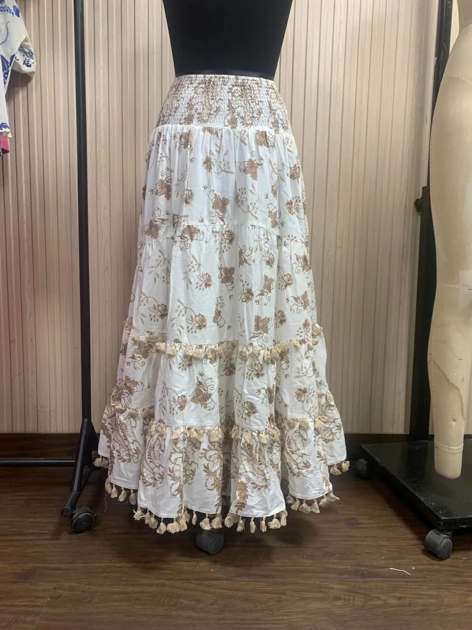 Front view of a white and gold tiered maxi skirt with tassel fringe on a dress form