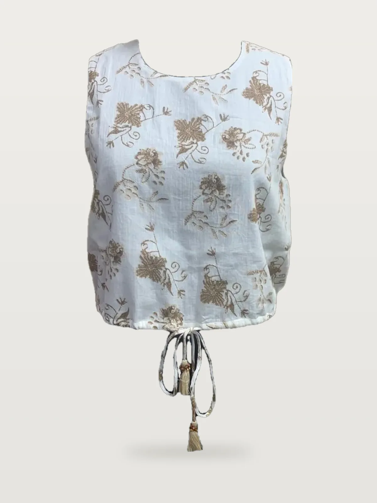 Front view of a white and gold embroidered sleeveless crop top with drawstring on a dress form