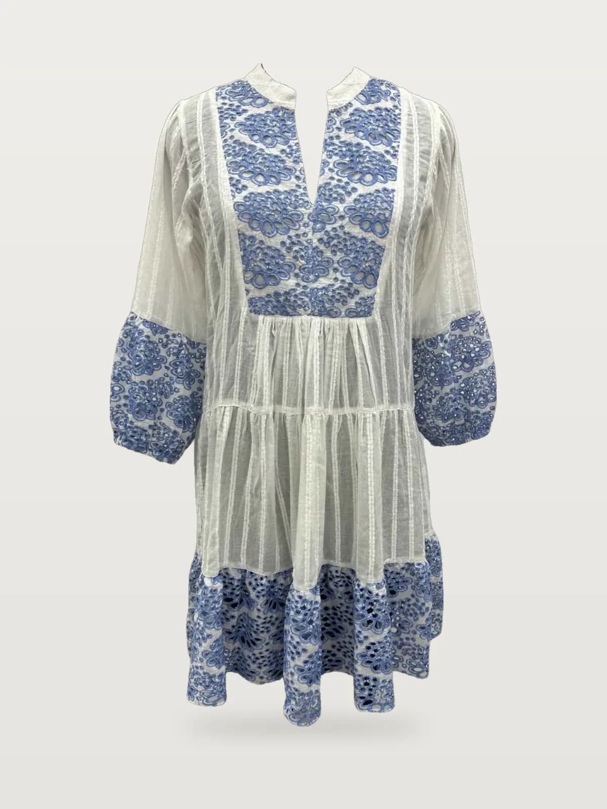Front view of a white and blue embroidered tiered tunic dress with bell sleeves on a dress form