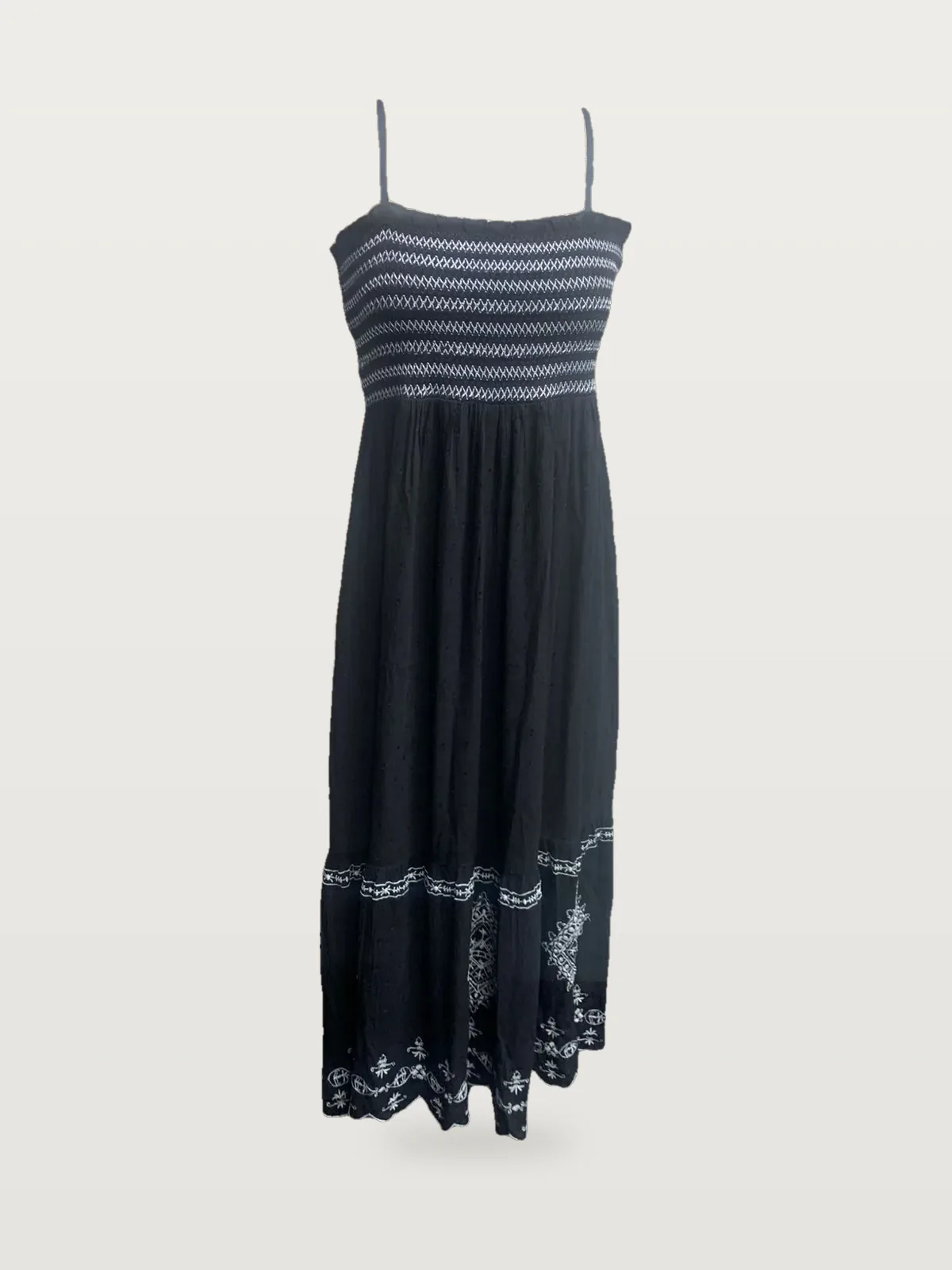 Front view of a black smocked strappy maxi dress with embroidered hem on a dress form