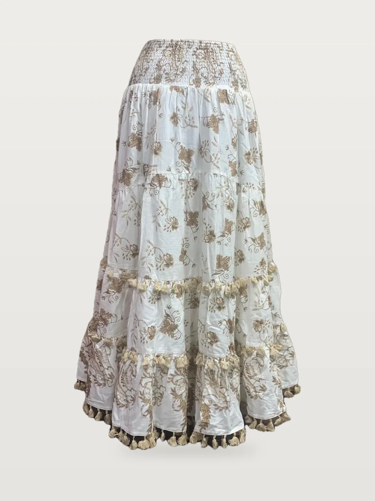 Front view of a white and gold tiered maxi skirt with tassel fringe on a dress form