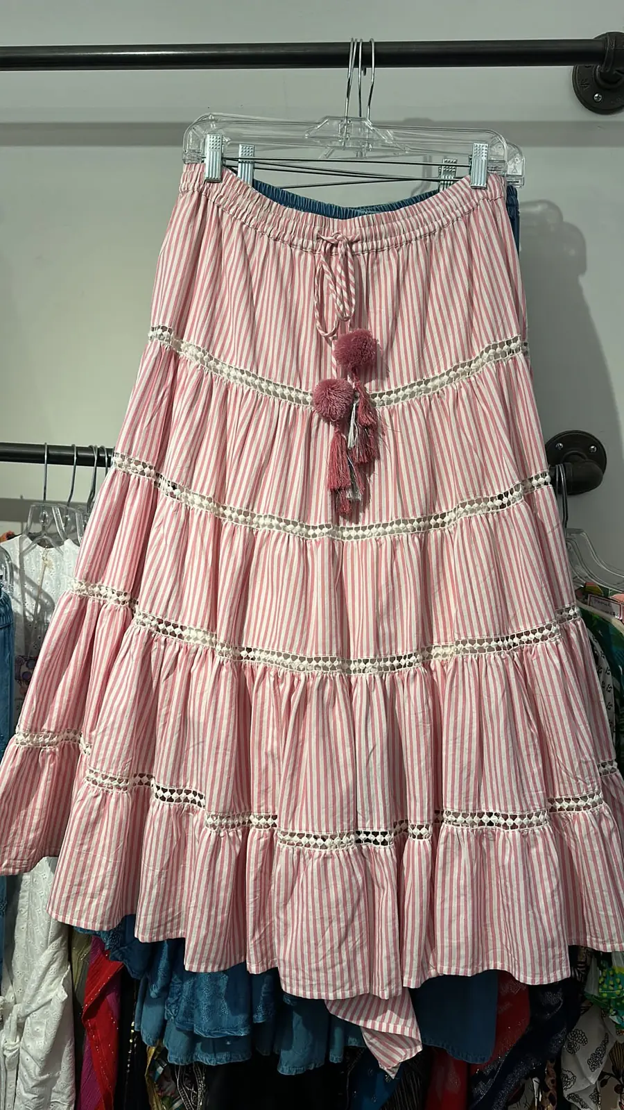 Front view of a pink stripe striped tiered maxi skirt with lace and pompoms on a hanger